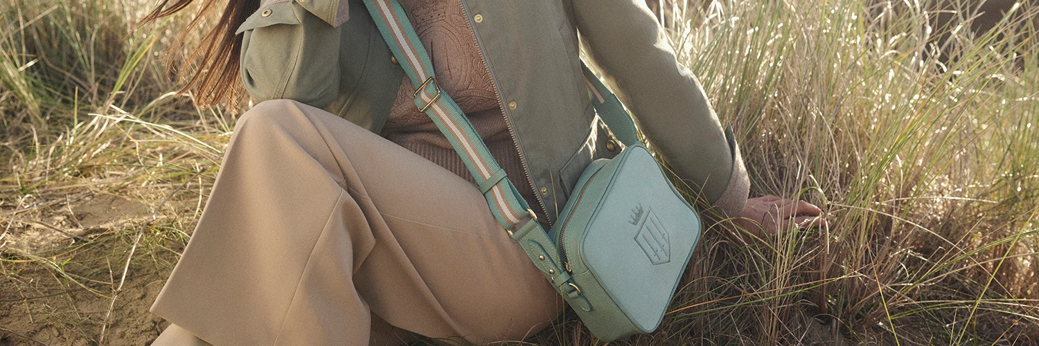 Fairfax & Favor Mint Collection at Wadswick Country Store. Women pictured sitting in field wearing Farifax & Favor Olivia Jacket and Mini Finsbury crossbody bag.